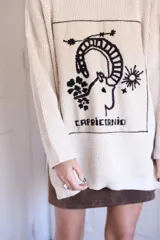 Sweater de punto oversize color crudo, con cuello redondo y diseño bordado a mano en el frente representando al signo Cáncer con un cangrejo, un corazón y una estrella.