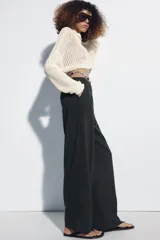 Pantalón de lino negro de tiro medio, con pernera recta, pinzas delanteras y detalle de puntilla en la cintura. Cuenta con bolsillos frontales y cierre con cremallera y botón.