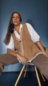 Chaleco tejido color tostado con destellos de lurex, escote en V y cierre frontal con botones. Presenta detalles de bordados y terminaciones en crochet en color crudo.