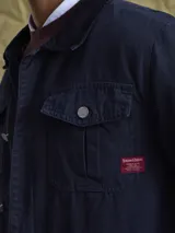 Campera de gabardina color azul marino, con cuello camisero, cierre frontal con botones metálicos y bolsillos frontales con solapa.