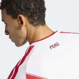 Camiseta de fútbol Adidas de la Selección Peruana, modelo Primera Equipación 26. Diseño principal blanco con una franja diagonal roja con textura geométrica que cruza el pecho, donde se ubica el escudo de la FPF. Presenta cuello en V y tres franjas rojas en los hombros.
