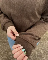 Buzo de punto texturizado en color marrón, de corte clásico con cuello redondo, mangas largas y puños y cintura elastizados. Incluye una pequeña etiqueta blanca con la marca en el borde inferior.