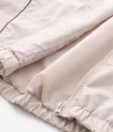 Campera de tejido técnico color beige con detalles de costuras en contraste color marrón. Presenta cuello alto, cierre frontal con cremallera, mangas largas con puños elásticos y estampa frontal con texto. Incluye un detalle bordado en la manga.