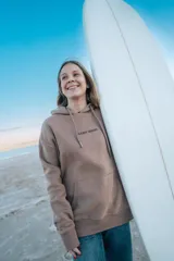 Hoodie marrón con capucha y cordón ajustable, con estampado en la espalda de un paisaje con palmeras, montañas y el texto "Glassy Waves".