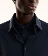 Camisa masculina de manga larga, cuello inglés y cierre frontal de botones, confeccionada en poliamida con elastano y tecnología performance.
