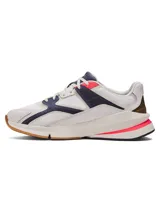 Championes Under Armour modelo Forge 96 Lthr Rissue, de diseño retro inspirado en los años 90. Combinan parte superior de malla y cuero en color blanco, con detalles en azul marino, toques de rosa fuerte y talón dorado. Cuentan con una entresuela robusta y suela de goma.