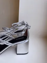 Sandalias plateadas de cuero nobuk, con tiras finas cruzadas en el empeine y tobillo, ajuste de pulsera y taco cuadrado de 7 cm.