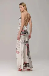 Vestido largo de satén con estampado tipográfico en tonos negro y rojo sobre fondo blanco. Presenta escote degagê, breteles finos y una caída fluida que estiliza la figura.