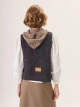 Chaleco de punto con capucha, confeccionado en lana. Presenta un diseño bicolor con cuerpo en tono beige de textura acanalada y capucha en tono marrón. Incluye una etiqueta de cuero en la parte posterior.