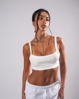 Top crop blanco de tirantes anchos, con escote recto y detalle de strass en el frente con el texto "Javastudio".