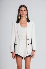 Blazer de corte sastrero en color marfil con detalles en negro en solapas, laterales y bolsillos. Presenta cierre frontal con dos botones y diseño estructurado.