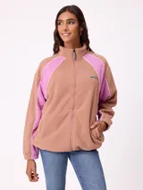 Campera de polar con cierre frontal, cuello alto y diseño de bloques de color en tonos tostado y fucsia con detalles de líneas blancas. Cuenta con bolsillos laterales y logo de la marca en el pecho.
