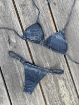 Conjunto de bikini azul oscuro con efecto desgastado o tie-dye sutil. El corpiño es de triángulos ajustables con tiras finas para atar al cuello y espalda, con copas removibles. La bombacha es vedetina con tiras laterales finas ajustables mediante hebillas metálicas.