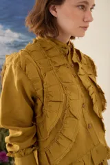 Camisa de lino color morado, con cuello mao, cierre frontal con botones y mangas largas con puños estructurados. Presenta detalles de volados frontales y ruedo con terminaciones desflecadas.