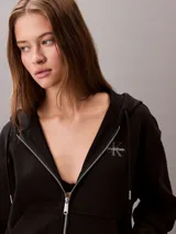 Buzo con capucha y cierre frontal de cremallera de la marca Calvin Klein, color negro, de corte regular cropped y manga larga. Presenta bolsillos tipo canguro, cordones ajustables en la capucha y el logo monograma de la marca estampado en el pecho.