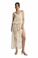 Vestido largo de encaje color beige, con escote en V y tirantes finos tipo halter. Presenta volantes en la parte superior y falda fluida con sutiles transparencias.