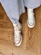 Zapatillas de lona color beige, tipo bota, con cordones marrones, puntera de goma y logo de peach engomado.