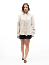Camisa de lino beige de manga larga, corte clásico y holgado, con cuello camisero y cierre frontal con botones.