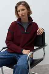 Sweater de punto grueso en color bordó, con cuello polo y cierre frontal parcial. Presenta detalles de vivos en color azul marino en el cuello, puños y hombros, con un diseño de corte holgado.