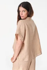 Camisa de lino marrón con mangas cortas, cuello mao con volados, cierre frontal con botones blancos y detalles de calados verticales en el frente.