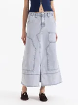 Pollera midi de denim en color azul claro con efecto lavado. Presenta un diseño de corte recto con costuras decorativas visibles, bolsillos frontales tipo cargo y una abertura central en el ruedo.