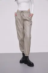 Pantalón tipo babucha de eco cuero color cemento, con cintura elástica y cordón de ajuste, bolsillos laterales y puños elásticos en los tobillos.