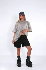 Remera oversize de algodón color gris claro, con cuello redondo y manga corta. Presenta un pequeño logo bordado en azul en el pecho.