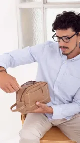 Neceser color marrón con dos divisiones independientes con cierre superior individual, ambas con bolsillos internos. Cuenta con un bolsillo frontal con broche magnético, un bolsillo trasero con cierre y un asa lateral.