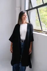 Poncho abierto de tejido de punto color negro, con mangas tres cuartos y bolsillos laterales.