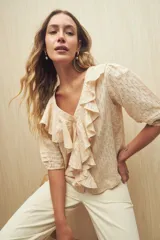 Blusa color crema con diseño calado, escote en V y volados frontales. Tiene mangas 3/4 con puños elastizados y cierre frontal con botones.