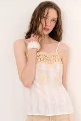 Musculosa blanca de tirantes finos con detalle de encaje y bordados en tono amarillo pastel en la parte superior y frontal.