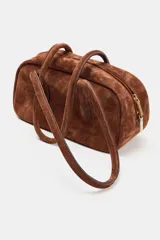 Bolso de hombro de formato alargado confeccionado en gamuza color marrón. Cuenta con doble asa de hombro y cierre superior mediante cremallera metálica.