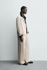 Pantalón de hombre de corte relajado, color beige claro, con cintura elástica, cierre frontal con botón y cremallera, bolsillos delanteros y bolsillos traseros de vivo.