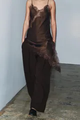 Pantalón marrón de tiro medio y corte carrot wide leg. Presenta trabillas en la cintura, bolsillos laterales ocultos en la costura, pespuntes marcados a tono y una hebilla decorativa en la espalda. Cierre frontal con cremallera, botón y ganchos metálicos.