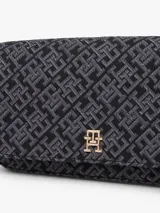 Cartera tipo mensajera de forma rectangular, con solapa frontal y correa ajustable. El cuerpo del bolso está confeccionado en jacquard con un patrón repetitivo del monograma TH en tonos negro y gris oscuro. Posee una insignia metálica dorada con el logo TH en el centro de la solapa.