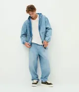 Campera bomber de jean en color azul medio, con cierre frontal de cremallera, capucha ajustable con cordones, bolsillos frontales y terminaciones elásticas en puños y cintura.