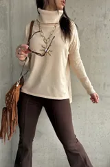 Polera de tejido de punto color beige, con cuello alto, mangas largas y aberturas laterales en el ruedo.