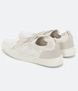 Zapatillas deportivas de punto color gris claro, con cierre de cordones y suela blanca.