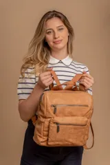 Mochila urbana de tamaño mediano confeccionada en símil cuero color crema. Presenta un diseño estructurado con asa superior, correas ajustables, un compartimento principal con cierre y un bolsillo frontal con cierre y detalle de costuras verticales.