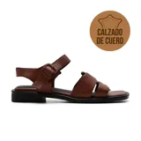 Sandalias bajas de cuero color marrón, con tiras anchas sobre el empeine, tira con hebilla al tobillo y suela plana.