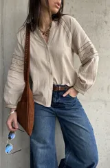 Camisa beige de inspiración boho con detalles bordados en mangas y puños, cuello en V con botones frontales y mangas largas abullonadas.