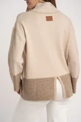 Polera de punto con diseño color block en tonos beige y marrón, de corte oversize, cuello alto y mangas largas con puños acanalados.