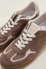 Zapatilla urbana de gamuza color marrón con detalles en beige, cordones claros y suela de goma tipo caramelo.