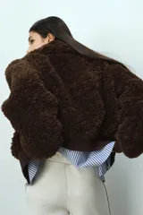 Campera corta de textura efecto peludito en color marrón oscuro. Presenta cuello alto, cierre frontal, bolsillos delanteros con solapa y puños y bajo en punto acanalado.