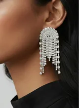 Caravanas de metal color plateado con diseño de cascada y flecos, recubiertas íntegramente de strass brillante. Cuentan con una base semicircular de la que se desprenden tiras colgantes de distintos largos.