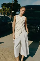 Top de algodón color crudo, con diseño sin mangas, cuello redondo y bajo asimétrico acabado en volante. Presenta frunces diagonales con detalles de cordones y cierre trasero con abertura y botón.