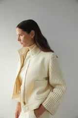 Campera de lana fina color crema, con cuerpo estructurado y mangas de tejido de punto acanalado. Presenta cuello alto, cierre frontal con botones y bolsillos laterales con doble abertura.