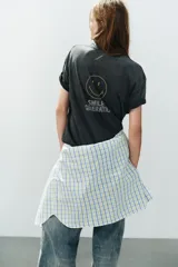 Camiseta oversize de algodón con efecto lavado, cuello redondo y manga corta. Presenta múltiples aplicaciones de brillos y strass con motivos coloridos de Smiley, incluyendo estrellas, corazones y caras sonrientes.