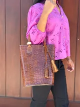 Matera de cuero con textura de cocodrilo en color tostado, con asas cortas y detalle de borla decorativa lateral.