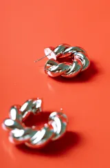 Aro tipo argolla de metal plateado con diseño trenzado.